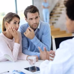 Pareja-sentada-en-clínica-de-fertilidad-frente-a-un-especialista-médico