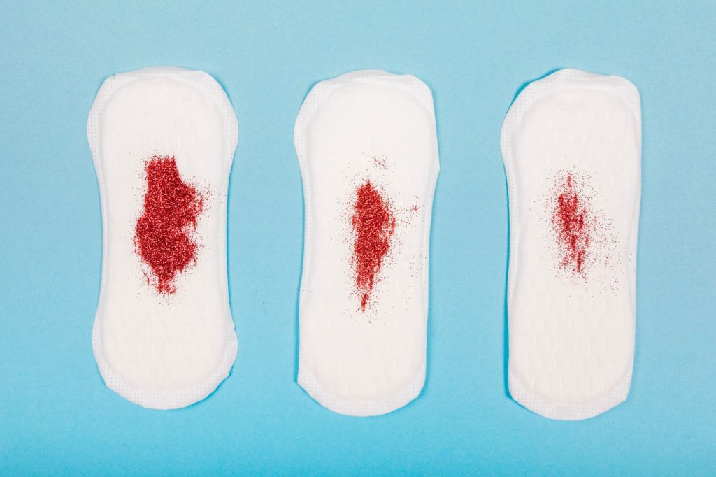tres-toallas-sanitarias-con-brillantina-roja-simulando-diferentes-flujos-de-menstruación-Three-sanitary-pads-with-red-glitter-simulating-different-menstrual-flows